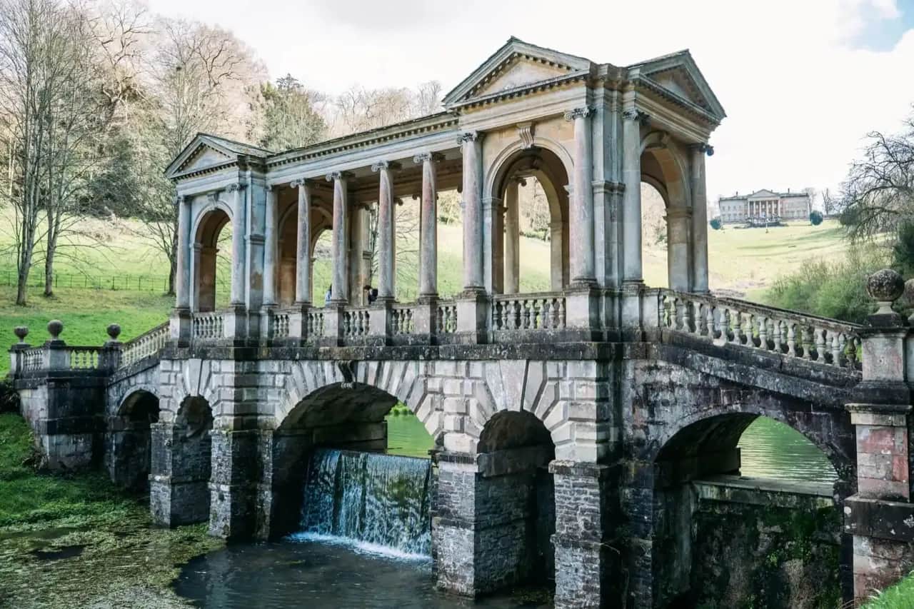 Stone bridge with a small waterfall, reminiscent of the English countryside in Jane Austen novels