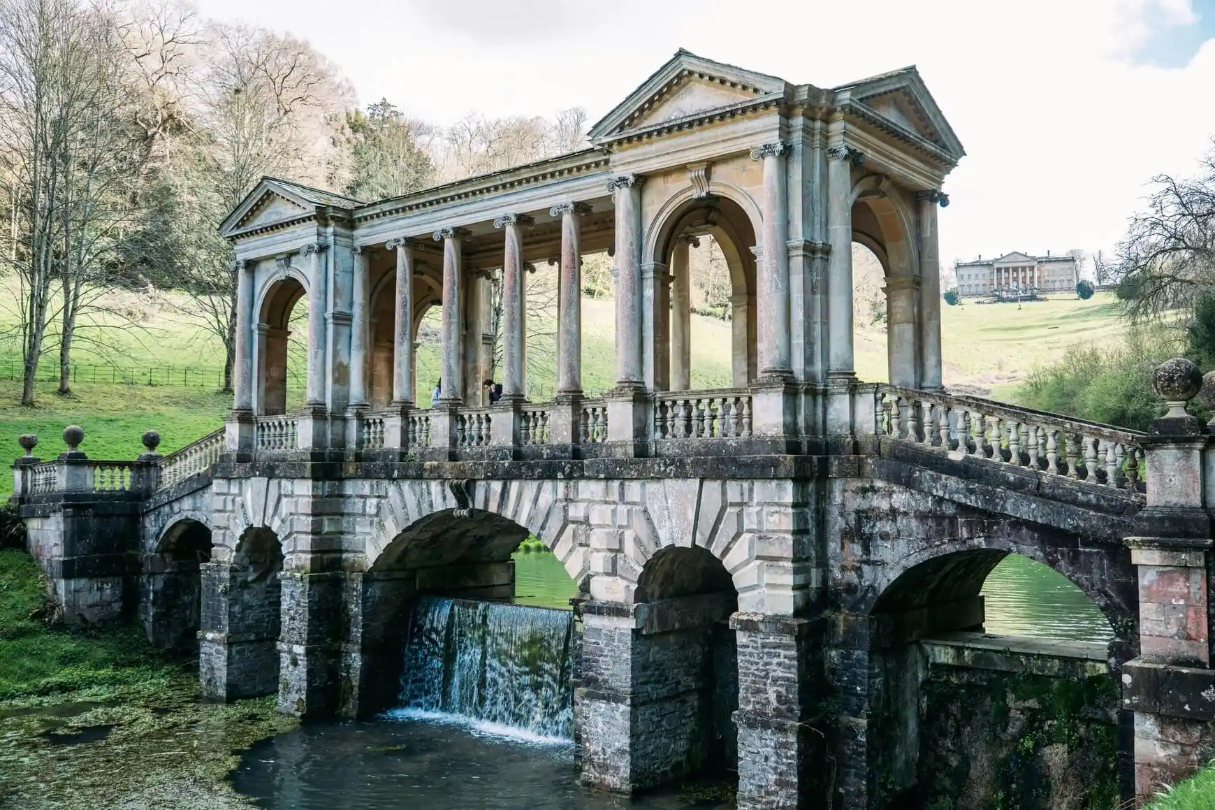 Stone bridge with a small waterfall, reminiscent of the English countryside in Jane Austen novels